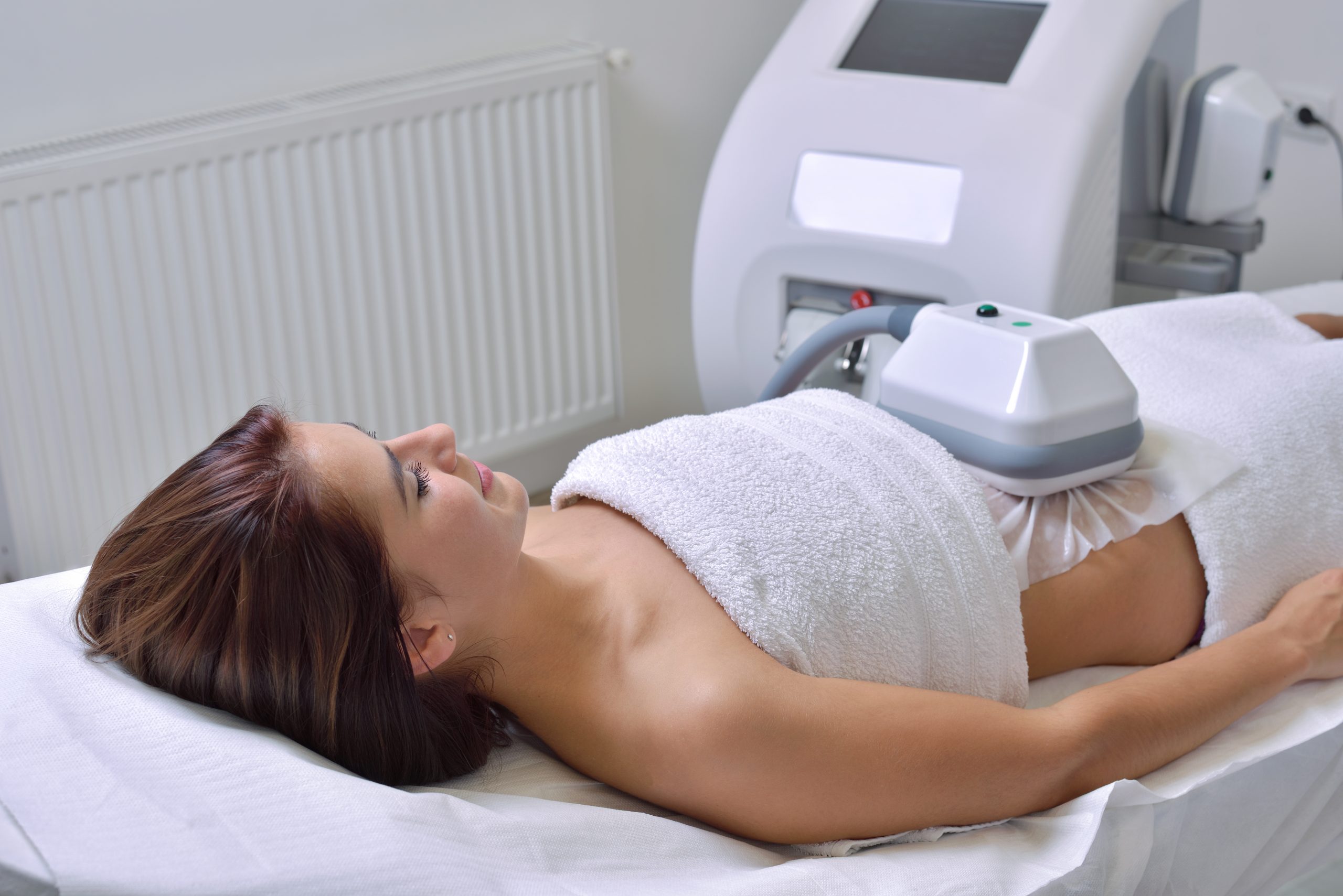 woman receiving coolsculpting treatment while laying on spa table and wearing a towel
