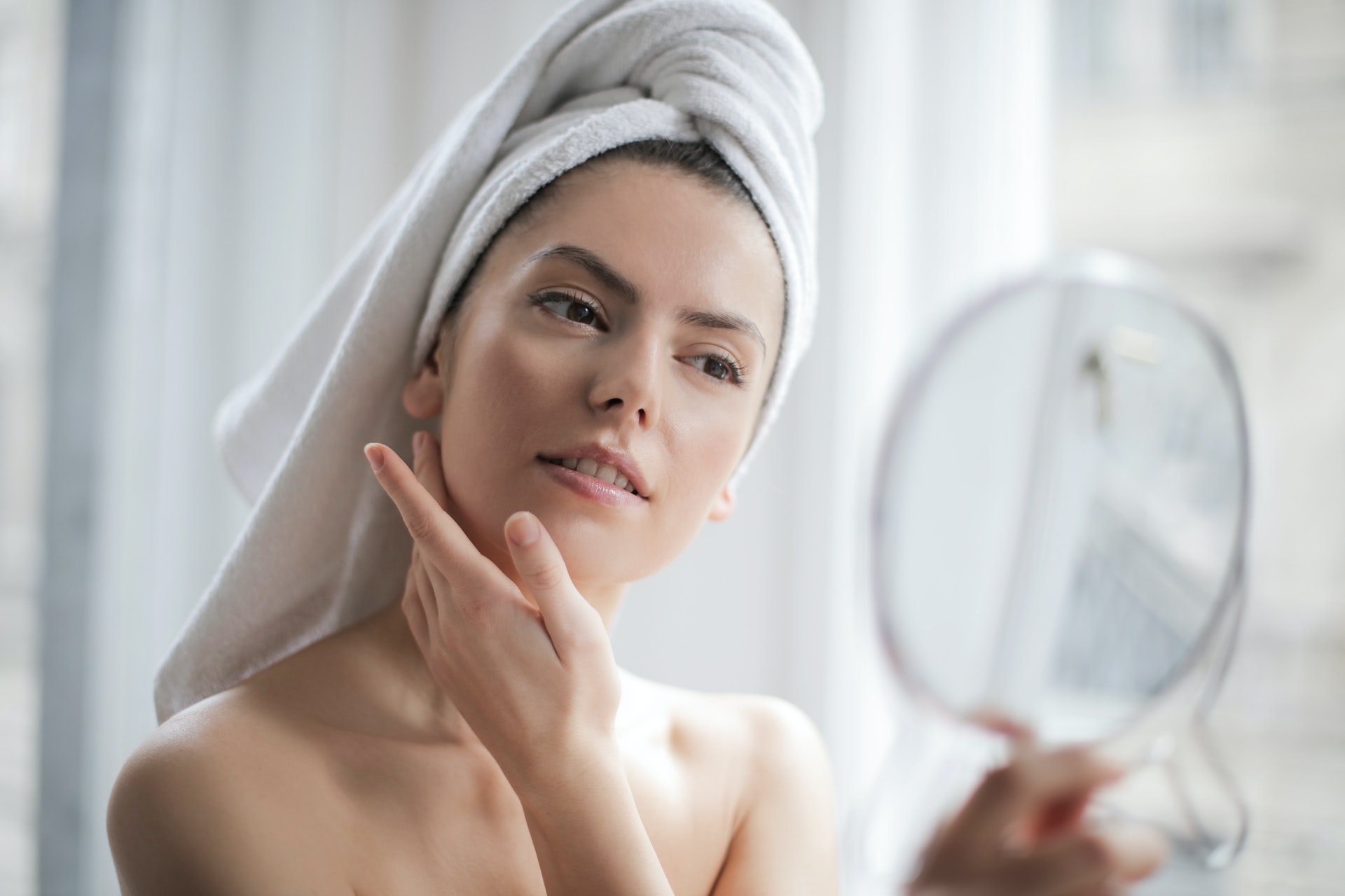 woman wearing towel in hair and touching face while looking at herself in a mirror